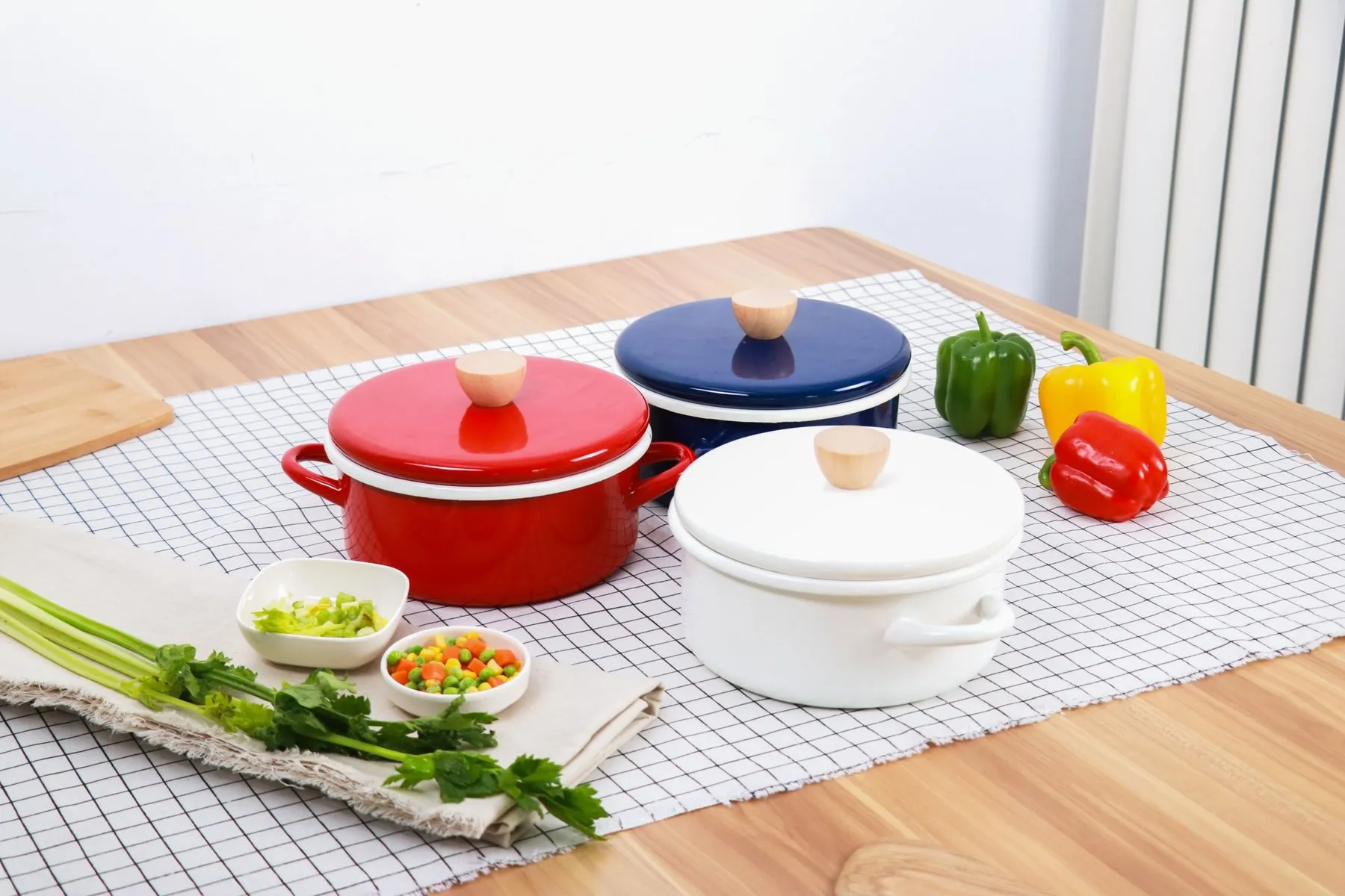 Red, cobalt and white enamel casserole pots with beech knobs on a checked cloth