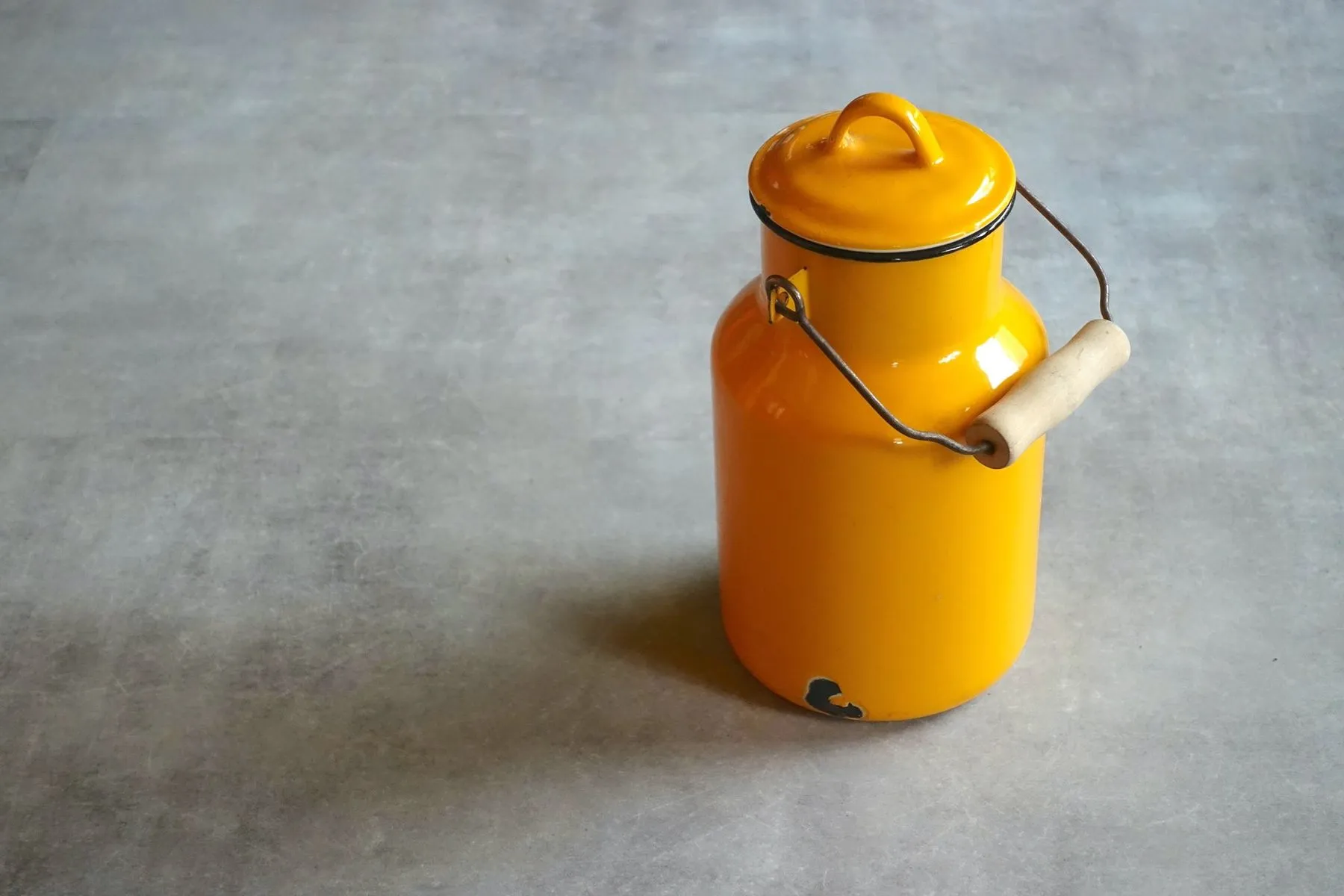 Mustard yellow enamel churn with a wooden handle on a concrete floor