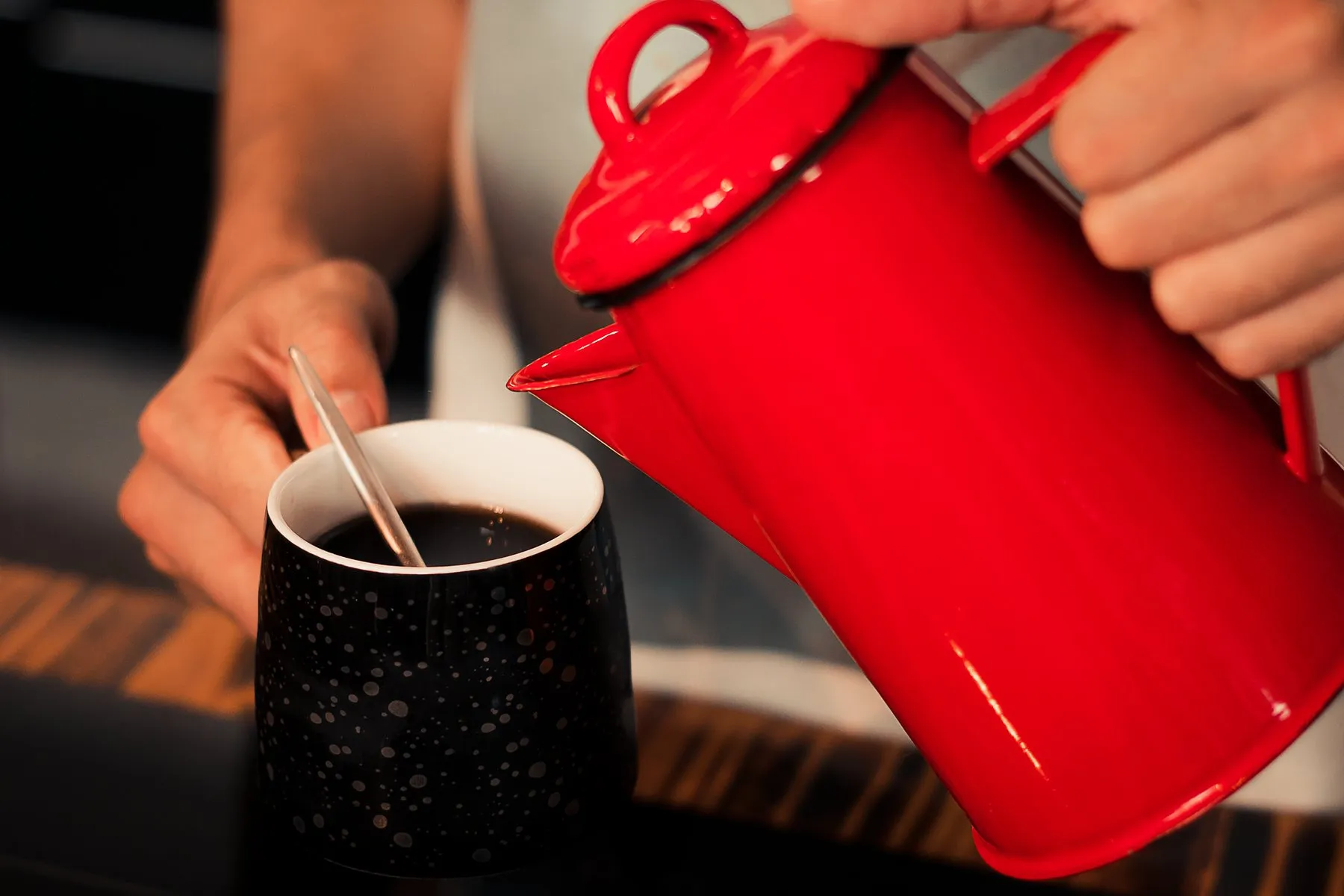 Coffee poured from an Iron Red enamel pot into a dark speckled cup
