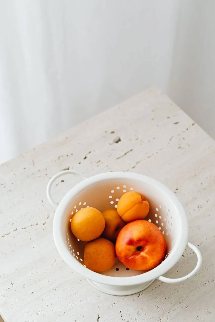 White enamel colander holding peaches and apricots on a stone worktop