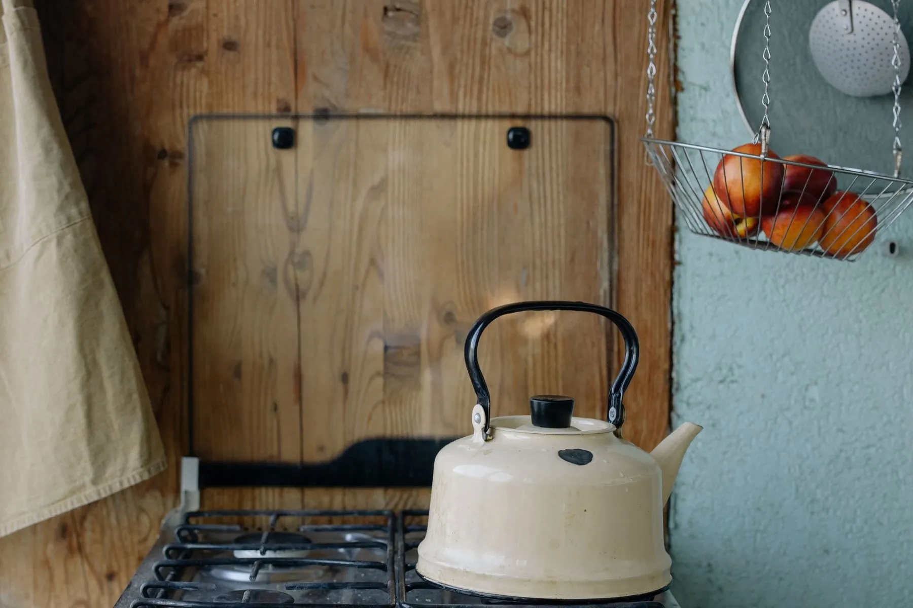 A cream enamel kettle on a gas hob against a wooden splashback