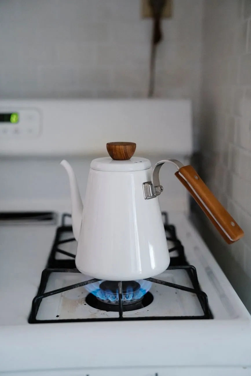 White enamel stovetop kettle with a wooden handle on a lit gas ring