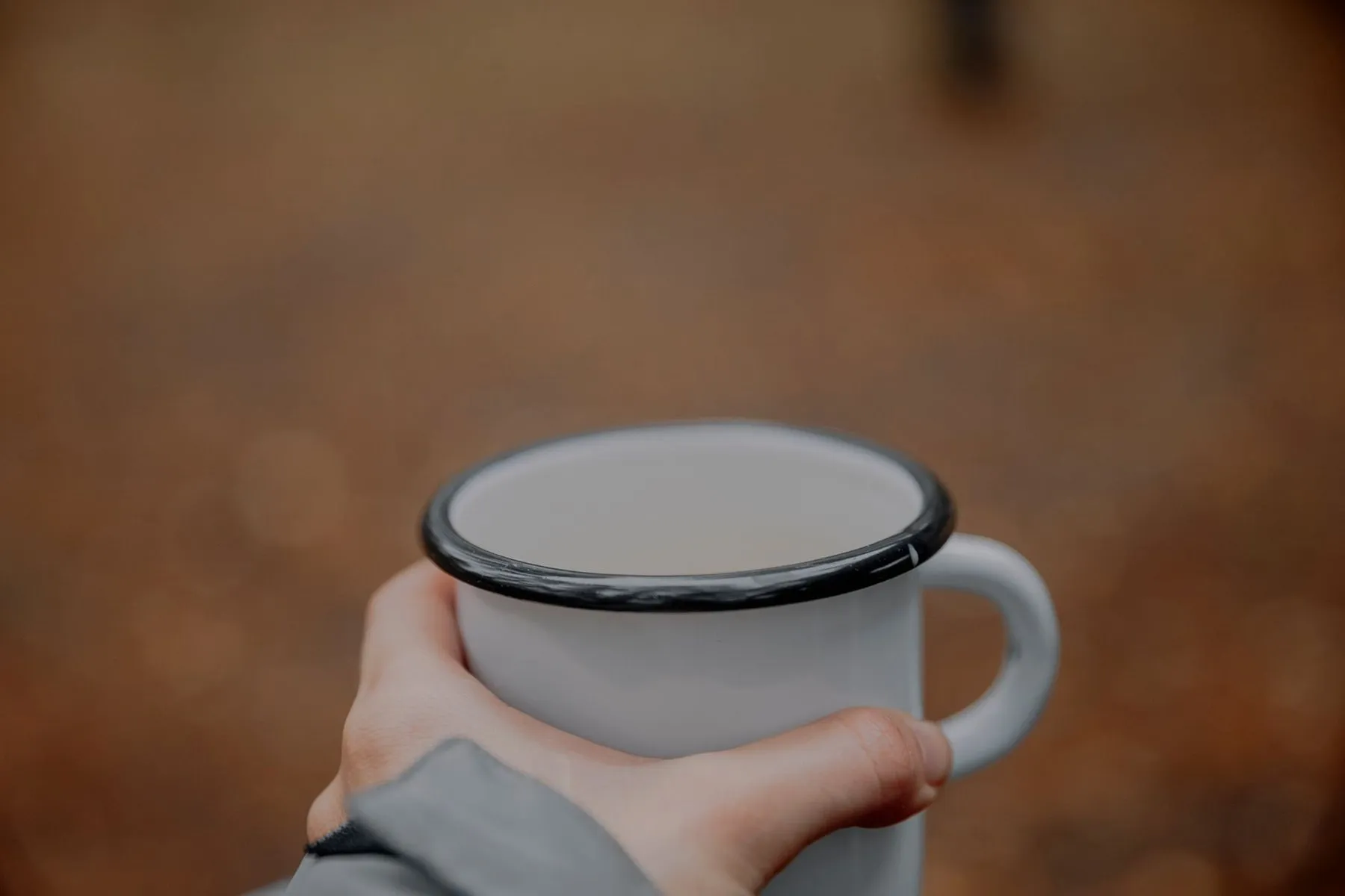 Two hands wrapped around an enamel mug outdoors
