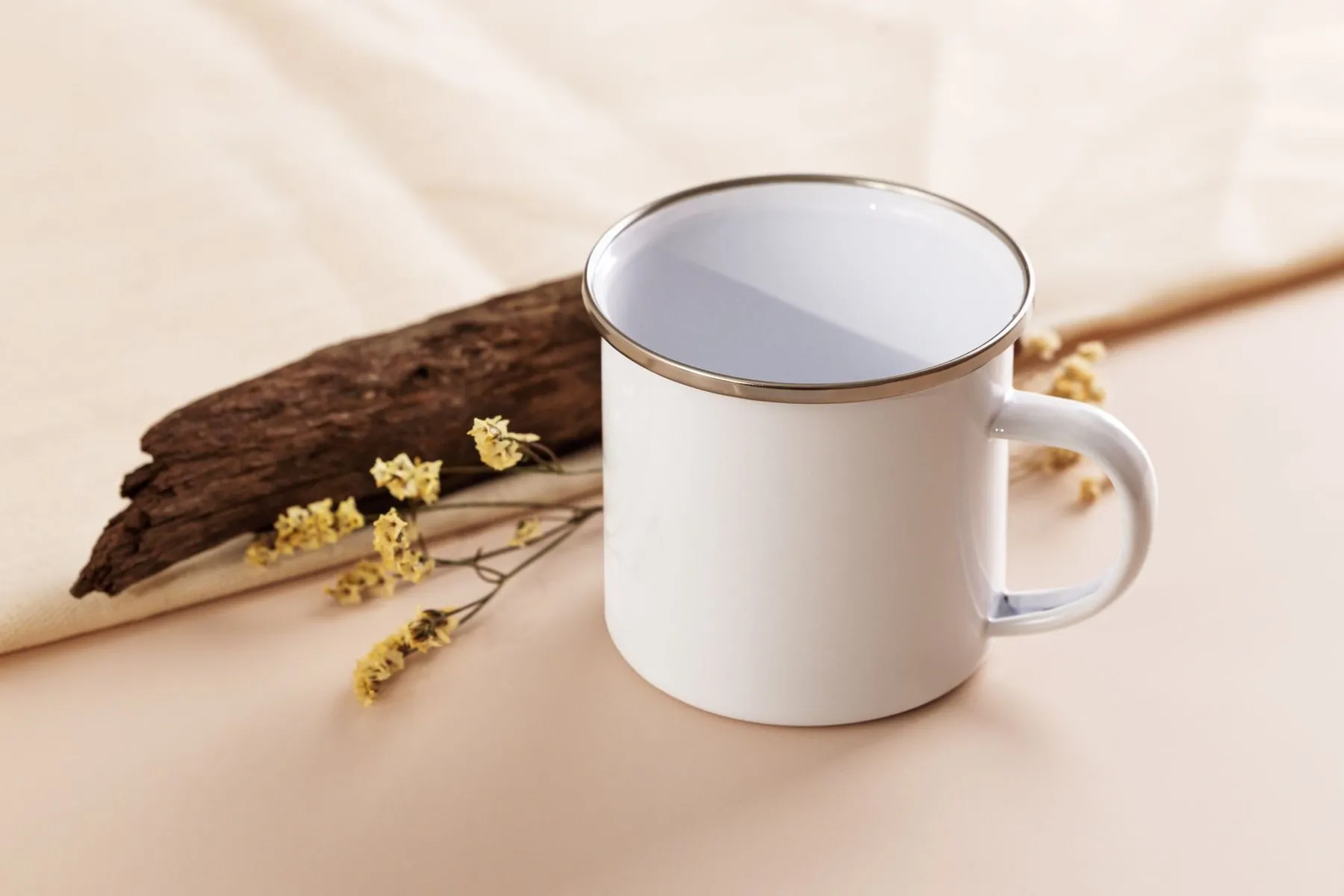 White enamel mug with a bright stainless steel rim beside dried flowers and driftwood