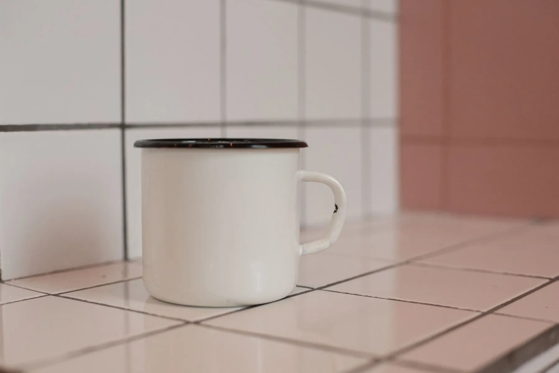 White enamel mug with a black rim on a pale tiled worktop