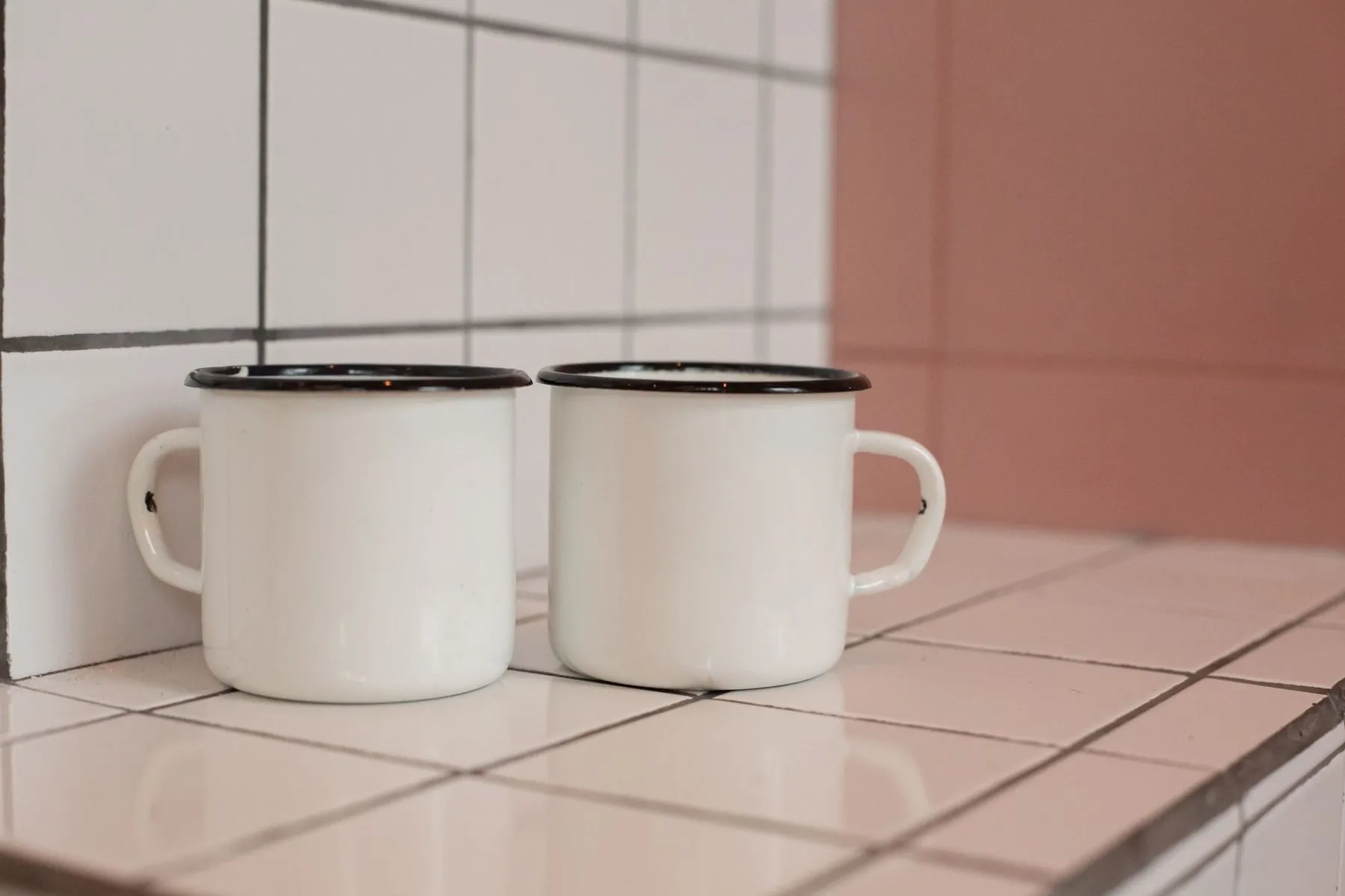 Two white enamel mugs side by side on a tiled worktop