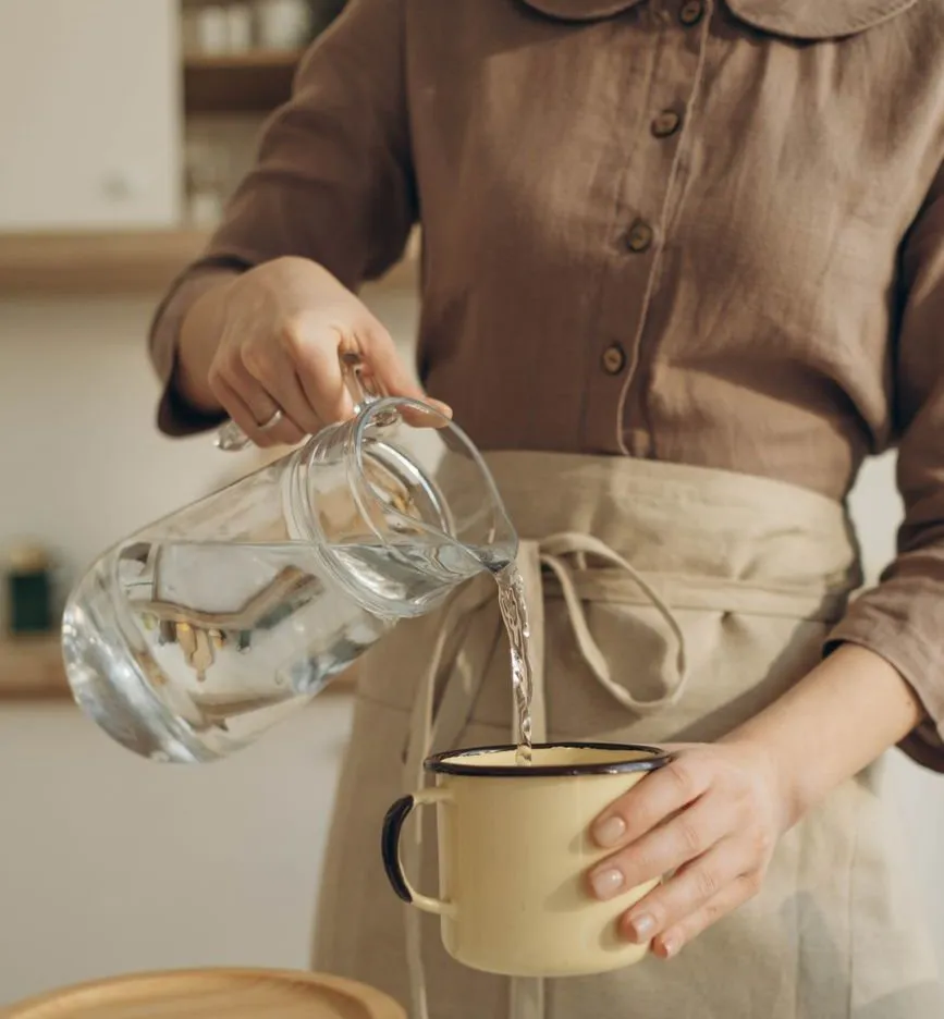 Water poured from a glass jug into a cream enamel mug held over a kitchen counter